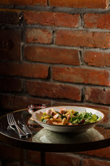 A salad with grilled salmon, mashed avocado and lettuce dressed with cream cheese. Close-up of the dish in a brown bowl isolated on brown background.