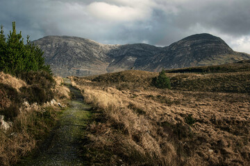 Dramatic cloudy landscape scenery with hiking trail and mountains in the background at Derryclare...