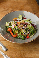 Greek salad with fresh vegetables: tomato, cucumber, red bel pepper, lettuce, onion, olives and cheese. Close-up on a white round plate on a wooden background. Salad menu with ingredients
