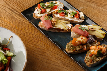 Bruschettas with vegetables. Start dishes with cherry tomatoes, avocado, cream cheese and shrimps. Food composition, tasty italian meal