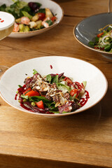 Salad with veal and tomatoes. Beef steak with raw vegetables mix side view. Grilled meat with garnish close-up. Delicious main course on table