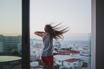 Girl with long hair stay on the balcony watch and dream. Summer time evening sunset, seaside.