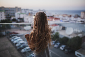 Fototapeta na wymiar Girl with long hair stay on the balcony watch and dream. Summer time evening sunset, seaside.