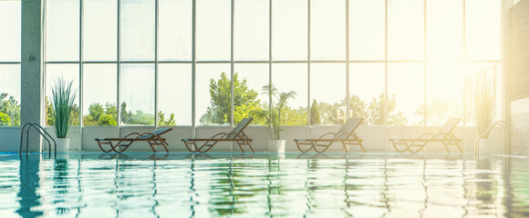 Water surface in empty spa hotel swimming pool with sun loungers for relaxation in sunlight, panorama horizontal banner with copy space.