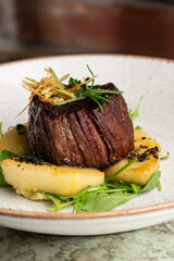 Grilled meat fillet steak medallion with green sauce, served with pear or apple. On dark background