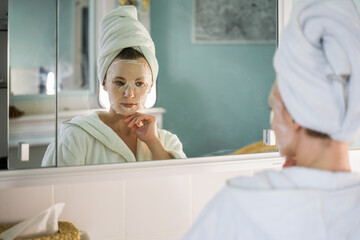 Calm woman wearing white towel is looking at the mirror and enjoying