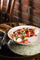 Prosciutto crudo ham salad with mozzarella cheese and arugula on a plate. Bright background. Top view. Copy space