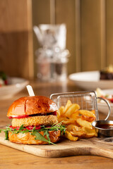 Big cheeseburger with french fries. Hamburger with beef patty onion, tomato, lettuce pickles, melted cheddar, mustards, tomato jam, mayo
