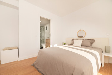 Bedroom with double bed with gray bedspread, white furniture and headboard, access to an en-suite toilet and light wooden floor