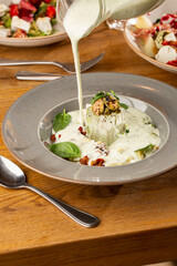 Closeup of cold soup okroshka with beef, vegetables and kefir served in a white bowl, selective focus. Summer, cold soup with cucumber, radish, egg, potatoes and fresh herbs seasoned with kefir.