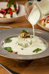 Closeup of cold soup okroshka with beef, vegetables and kefir served in a white bowl, selective focus. Summer, cold soup with cucumber, radish, egg, potatoes and fresh herbs seasoned with kefir.