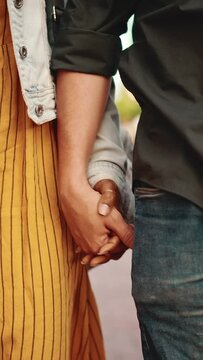 VERTICAL VIDEO: Closeup, man and woman walk holding hands. Close-up of the hands of a young interracial couple