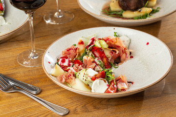 Prosciutto crudo ham salad with mozzarella cheese and arugula on a plate. Bright background. Top view. Copy space