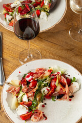 Prosciutto crudo ham salad with mozzarella cheese and arugula on a plate. Bright background. Top view. Copy space