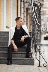 Young elegant man weared in black and white on background of City. Fashion style guy classic portrait. Street style male portrait looking to camera. Contemporary businessman. Modern urban walk in town