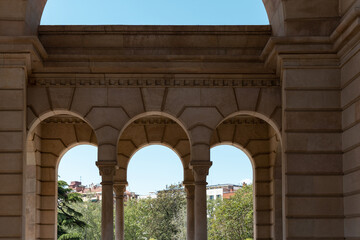 Arched stone columns with view of a town in the background. Wall of a building with arched openings