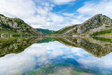 Lakes of Covadonga, Lake Enol, with the mountains and clouds reflected on the water, on a day with a cloudy sky and no wind.