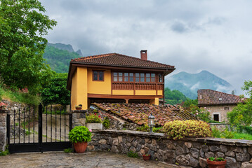 Typical house in the Asturian mountains, with a wooden balcony, surrounded by nature and flower pots on a cloudy day.