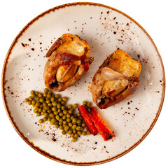 Two spicy baked quails with vegetable garnish of sweet carrots and canned green peas on plate....