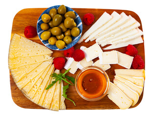 Different types of cheese sliced and served on board with little bowl of honey, marinated olives...