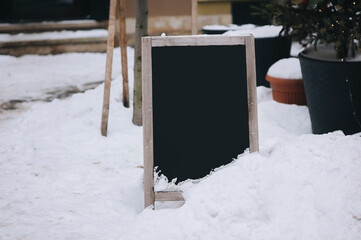 A vintage blank black wooden billboard stands on a winter snowy road. The concept of outdoor advertising for cafes and shops. Copy space, layout.