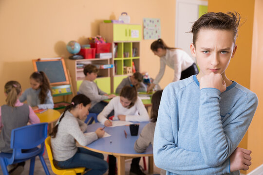 Portrait of sad schoolboy and children drawing in classroom