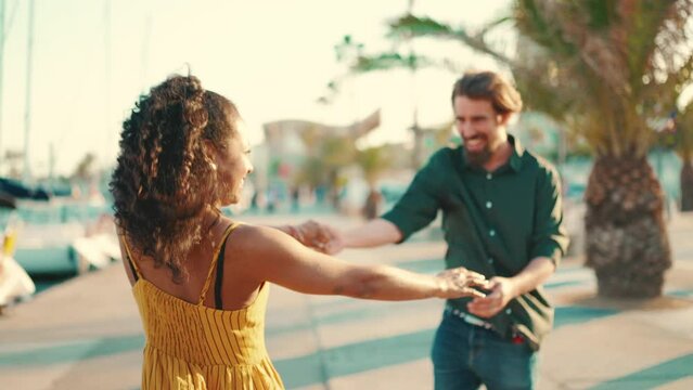 Close-up of young happy man and woman joyful dancing on the embankment on yacht background. Closeup, joyful date of a young interracial couple.