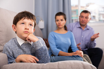 Portrait of offended boy after quarrel with parents sitting on sofa at home