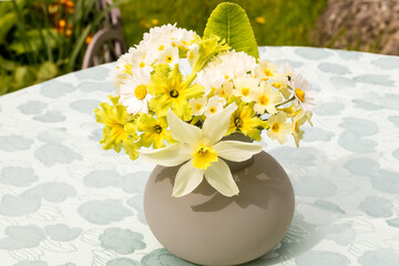 A summer bouquet of various light pastel flowers in a small glass vase on a table in the garden.