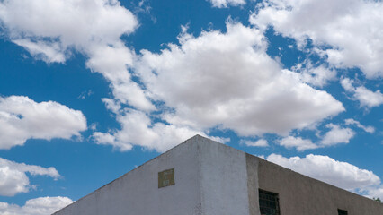 CIelo azul con nubes blancas sobre muro rustico de yeso blanco y cemento