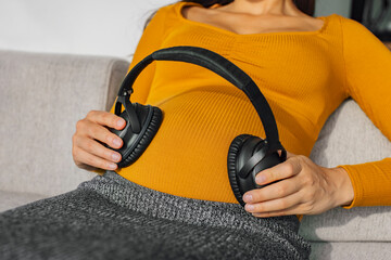 Headphones on pregnant stomach for music listening during pregnancy. Woman holding earphones to...