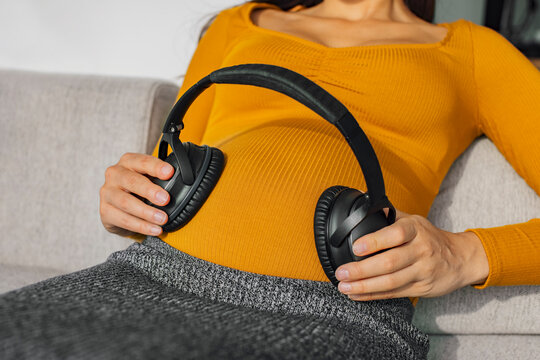 Headphones on pregnant stomach for music listening during pregnancy. Woman holding earphones to foetus for brain development