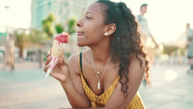 Closeup portrait of smiling woman with long curly hair with ice cream in her hands on an urban city background. Frontal close-up of a happy girl testing ice cream on a warm sunny day