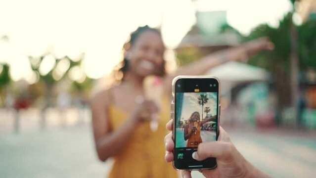 Close-up of a man taking a picture of a woman on a mobile phone. Closeup, smiling woman eating ice cream and filming it with smartphone on urban city background. Backlight