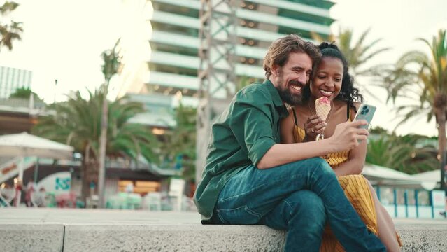 Close up portrait of happy man and smiling woman watching video on smartphone. Close-up of a joyful young interracial couple browsing photos on a mobile phone on urban city background