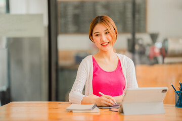Asian female student studying online, e-learning with tablet sitting at desk and holding pen, happy Asian elementary school girl smiling at camera, thinking about distance learning.