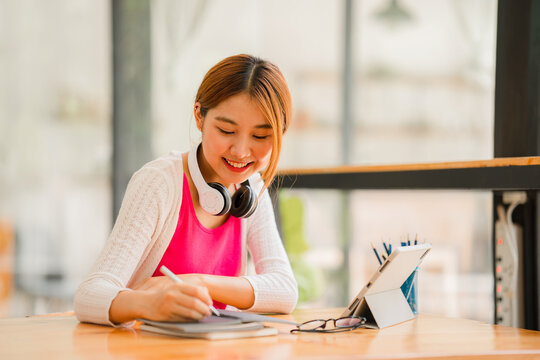 Asian female student studying online, e-learning with tablet sitting at desk and holding pen, happy Asian elementary school girl smiling at camera, thinking about distance learning.