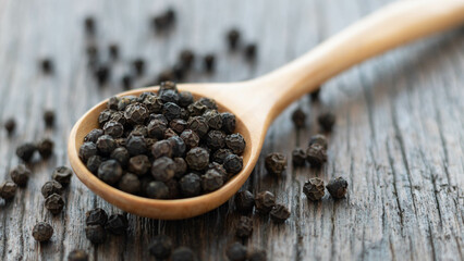 Whole black peppercorn in a wooden spoon on wooden background.