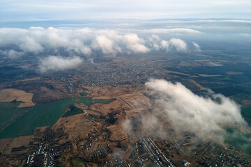 Aerial view from high altitude of distant city covered with puffy cumulus clouds forming before...