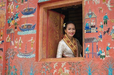 Asian Laos female lady wearing traditional Lao costume smile friendly and posing in an ancient temple with beautiful wall in Luang Prabang - one of the travel city in Laos, ASEAN