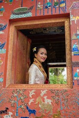 Asian Laos female lady wearing traditional Lao costume smile friendly and posing in an ancient temple with beautiful wall in Luang Prabang - one of the travel city in Laos, ASEAN