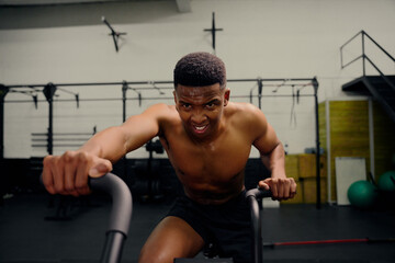 Fototapeta na wymiar African American male using an elliptical trainer during cross fit training. Male athlete exercising intensely in the gym. High quality photo