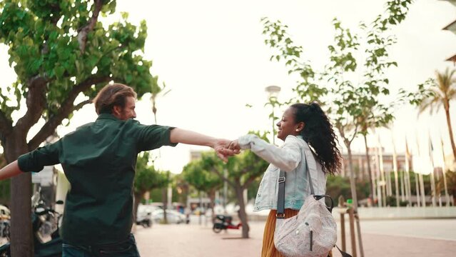 Closeup, happy interracial couple going down the alley holding hands and dancing. Close-up of young happy man and woman joyful dancing on the city street  