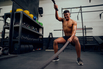 Fototapeta premium Young African American male exercising inside a gym. Mixed race male personal trainer using rope to strengthen his arms. High quality photo