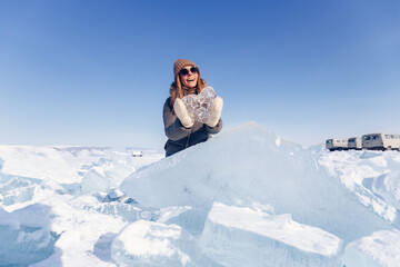 Fototapeta na wymiar Happy tourist in sunglasses holds crystal clear ice on background of winter lake Baikal