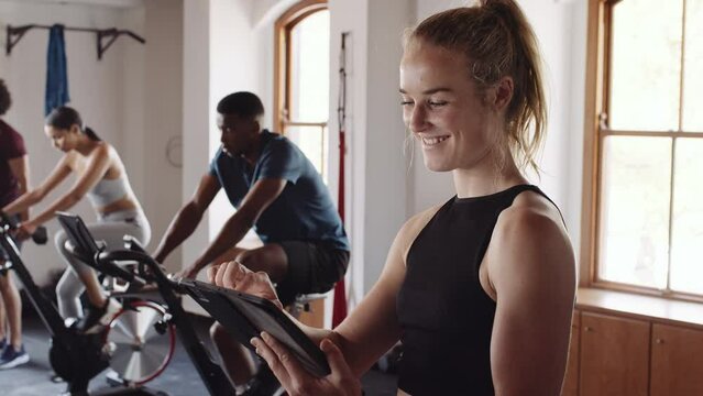 Happy young adult Caucasian female confidently smiling and using electronic tablet at an indoor fitness gym