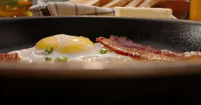 Putting frying pan with freshly fried eggs and bacon on table with served nourishing balanced breakfast - morning meal preparation 4k footage