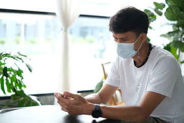 Thai man wearing the medical mask using his mobile phone and reading news about the situation with...