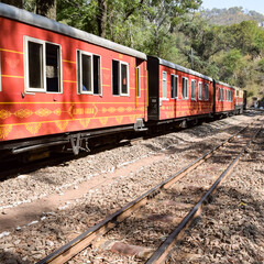 Obraz premium Toy Train moving on mountain slopes, beautiful view, one side mountain, one side valley moving on railway to the hill, among green natural forest. Toy train from Kalka to Shimla in India