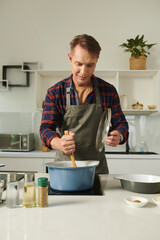 Man in plaid shirt and apron mixing sauce with wooden spatula